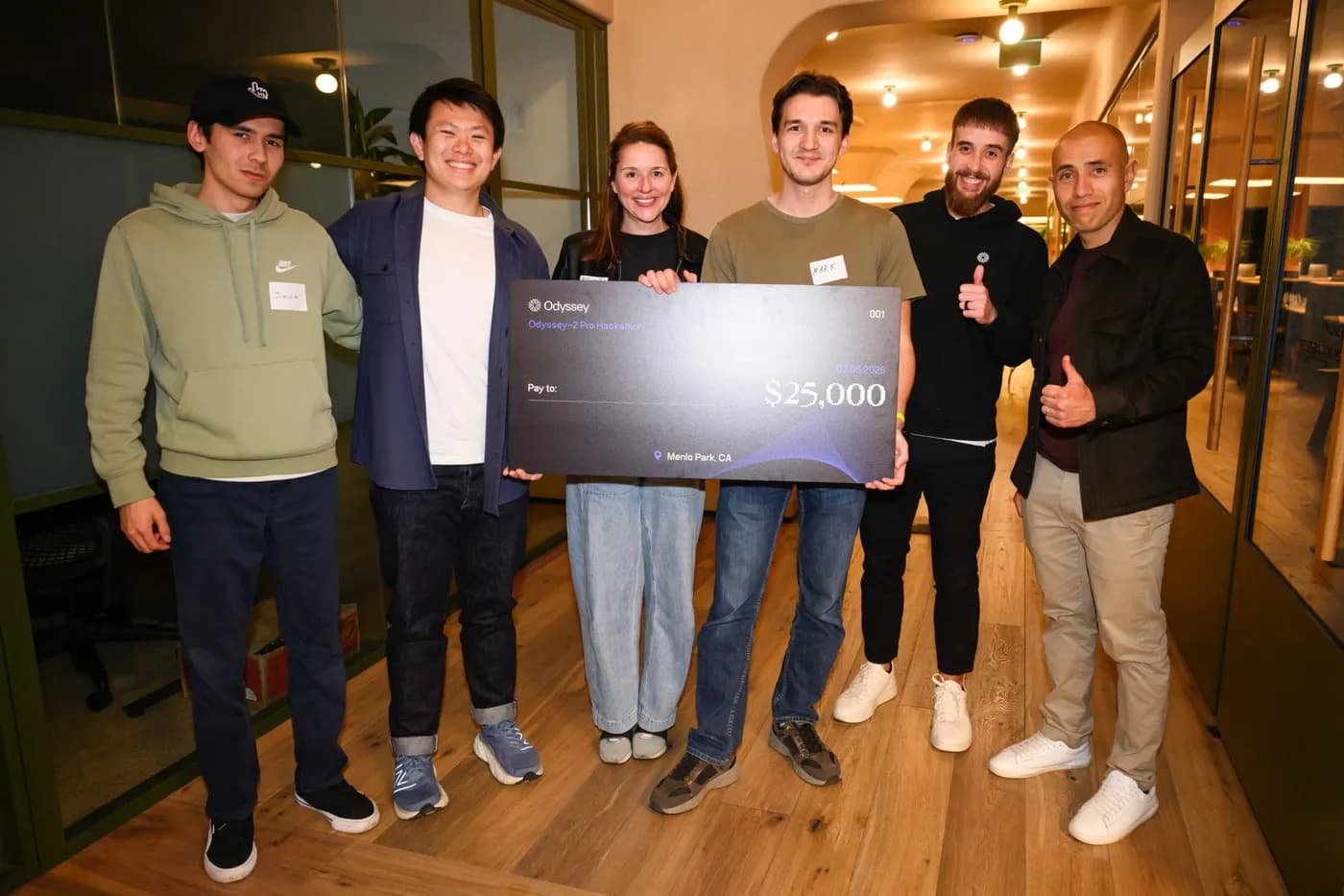 Javokhir Shomuratov and teammates holding the $25,000 Odyssey-2 Pro Hackathon winners' check with the OdysseyML team — Soleio, Oliver Cameron and Kristy McDonough